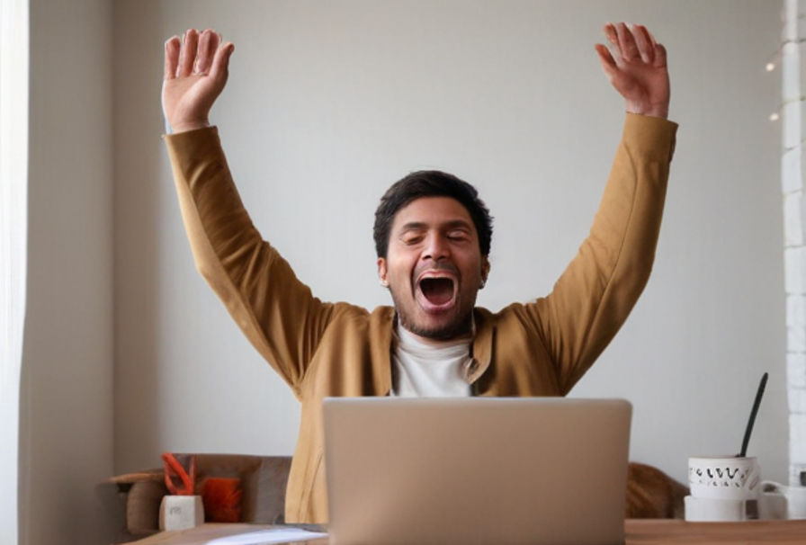 A man raising his hands celebrating in front of his laptop.