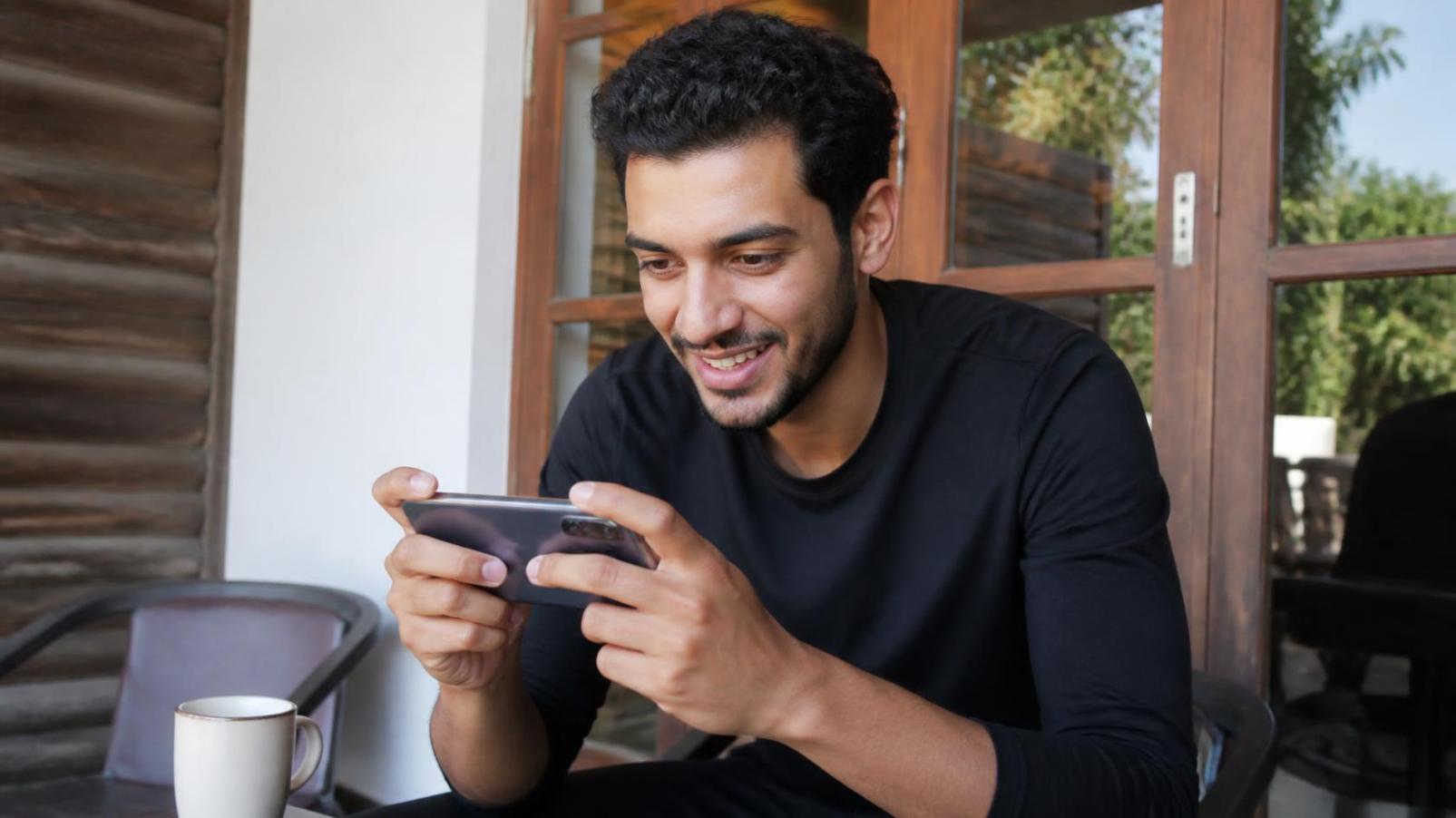 Young man smiling at phone outdoors, capturing genuine excitement during casual routine.
